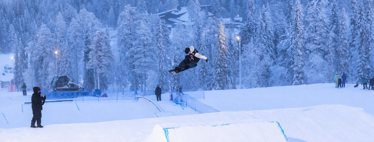 Snowboarder jumping above a snowy slope framed by winter forest